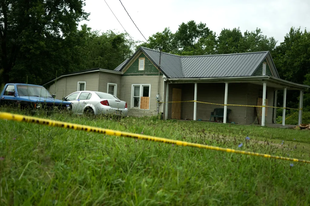 The Sider's home at 82 Ohmer St. in Hamden, Ohio, a single-story house with a porch and two cars parked in the grassy yard, marked off by yellow police tape in the foreground.