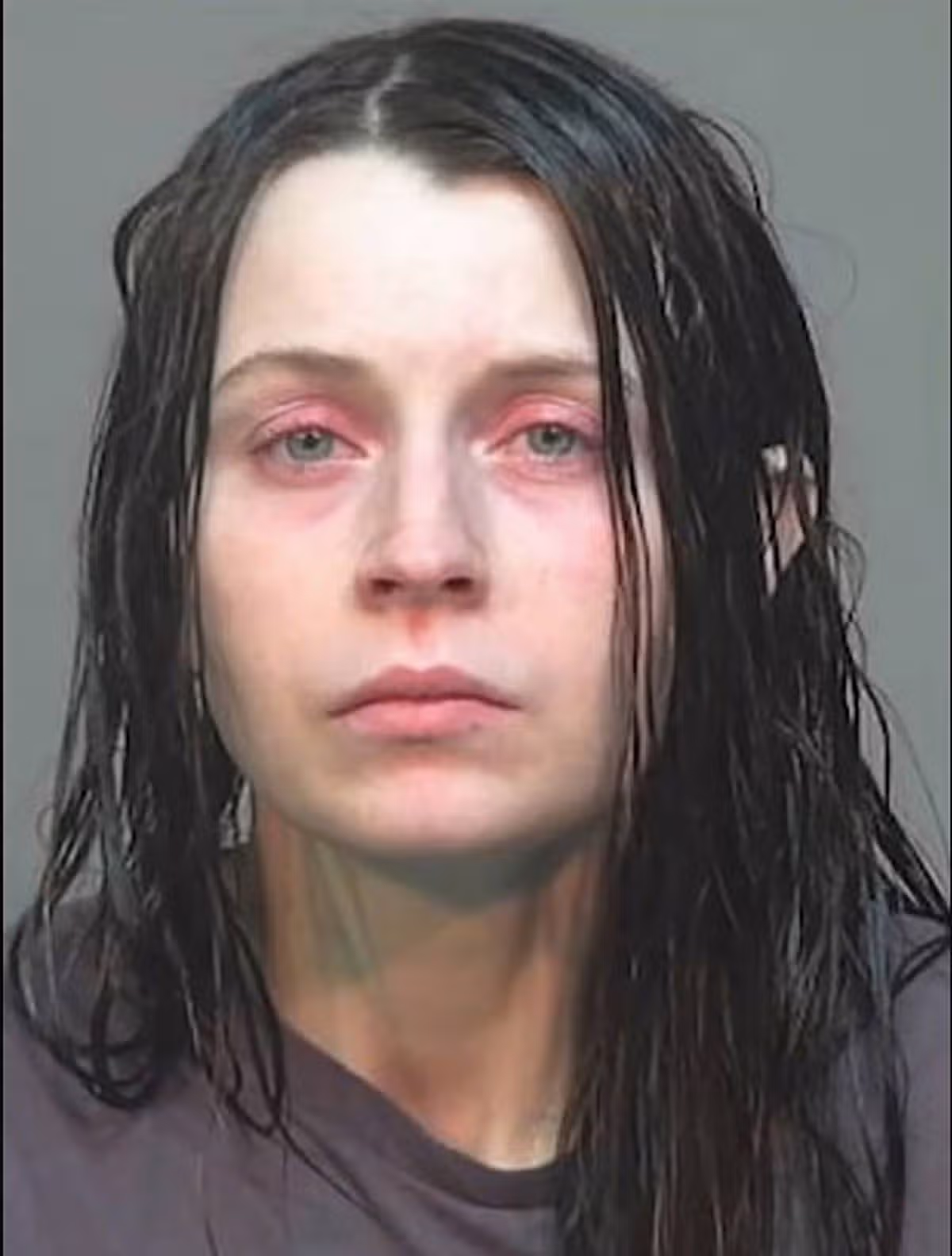 The image depicts a close-up portrait of an individual with long, dark hair. The person's face appears slightly flushed, with no