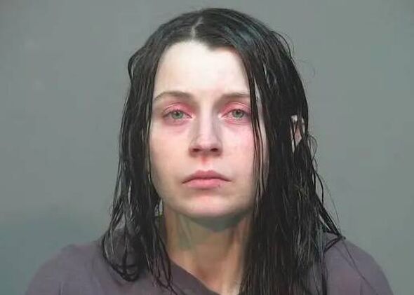 An individual with long, wet hair and a neutral expression stands against a gray background, likely in a law enforcement setting