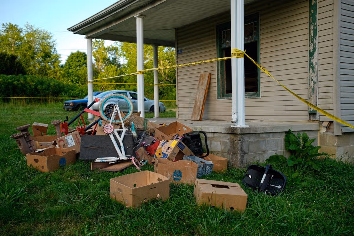 Police tape surrounds a home and debris is seen on the front lawn, including baby carrier, where authorities say they removed 16 children and arrested four adults in Hamden, Ohio, Wednesday, July 1, 2026.