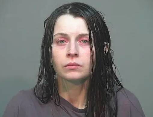 A photograph of an individual with long, dark hair, appearing to be in a formal setting, likely a law enforcement facility. The