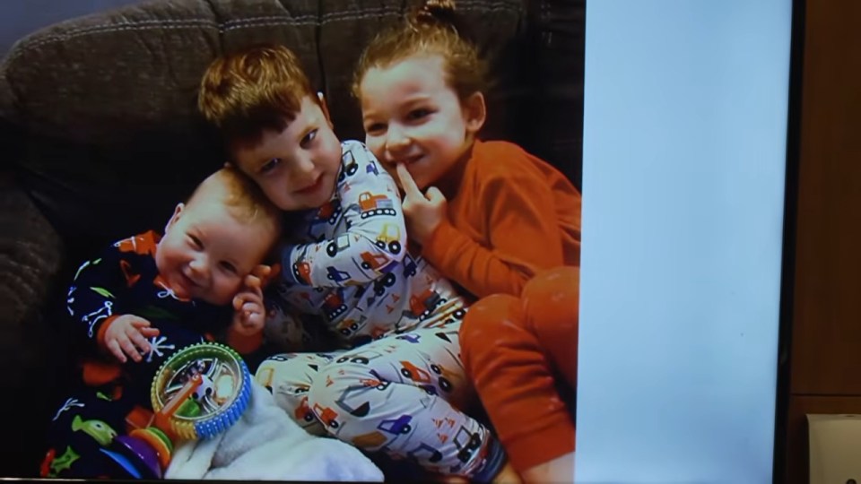 Three children smiling and dressed in pajamas, sitting together on a couch.