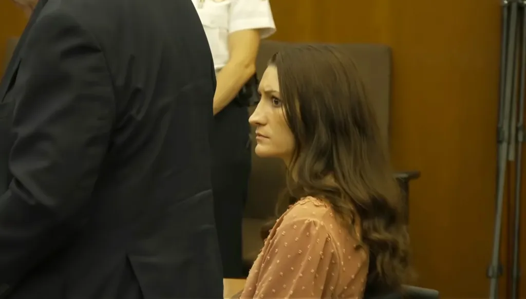Clancy wearing a light brown long-sleeve blouse and her brown hair is flowing down her back.