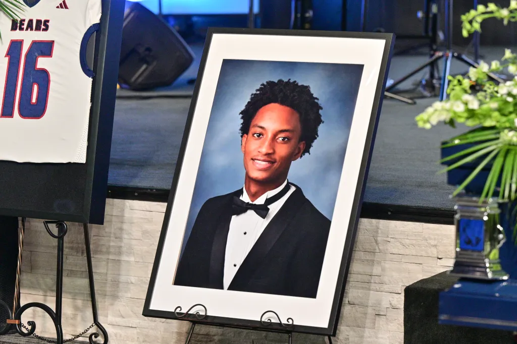 Funeral display with a photo of Nolan Wells in a tuxedo next to a white sports jersey with "BEARS" and "16" on it.