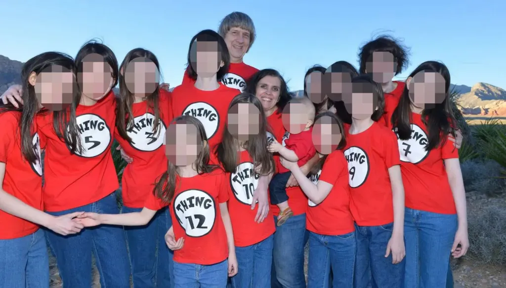 A family of 15, including parents and 13 children, all wearing matching red "Thing" shirts, stand outdoors.