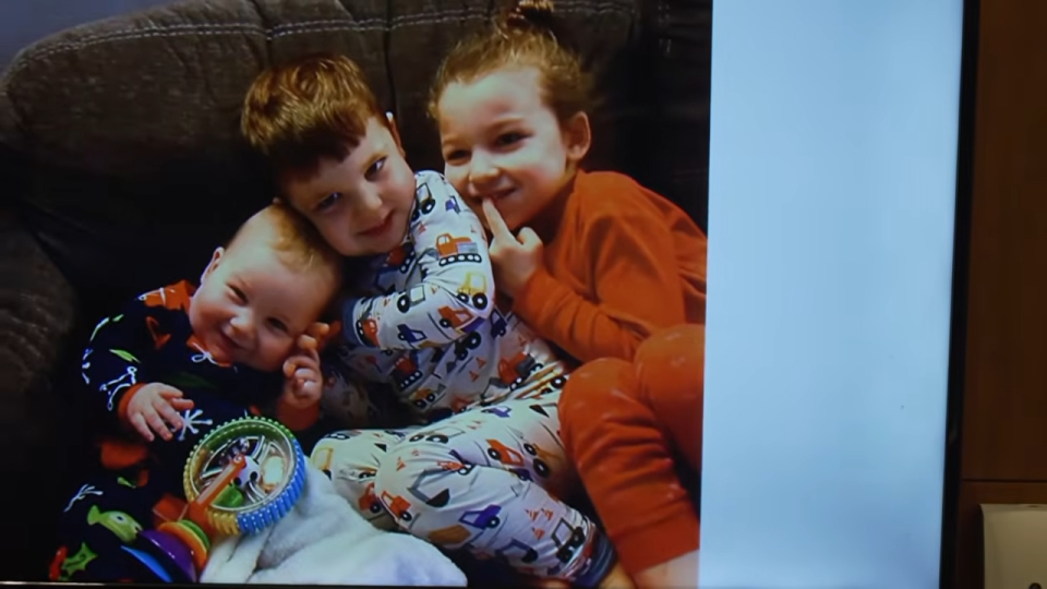 Three smiling children in pajamas sit close together on a couch.