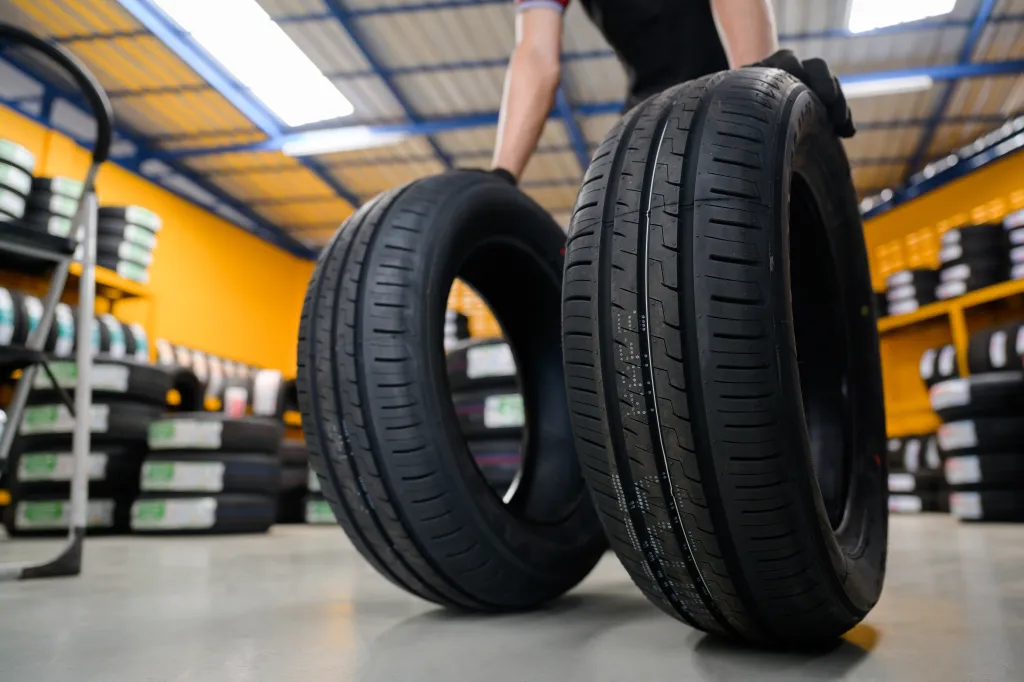 A mechanic in a tire warehouse holds two new tires in a low-angle shot.