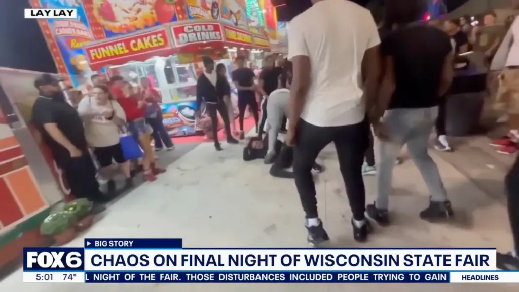 A fight at the Wisconsin State Fair, with people in the foreground and a funnel cake stand in the background.