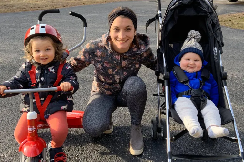 Lindsay Clancy smiling between two children, one on a tricycle and one in a stroller.