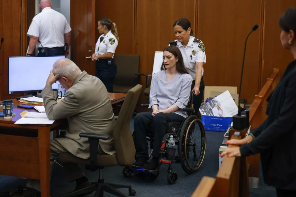 Lindsay Clancy in a wheelchair, escorted by an officer, at her murder trial.