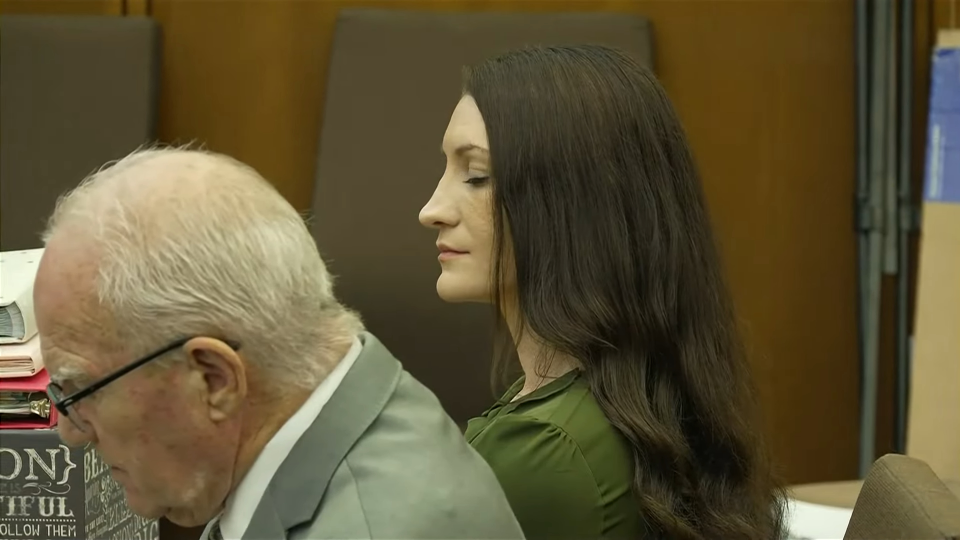 Lindsay Clancy, with long brown hair, sitting in court with a man next to her.