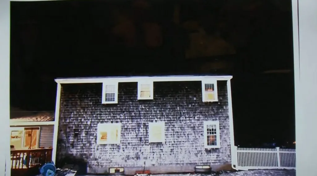 A house with dark shingles and white windows, taken at night, with light visible through some windows.