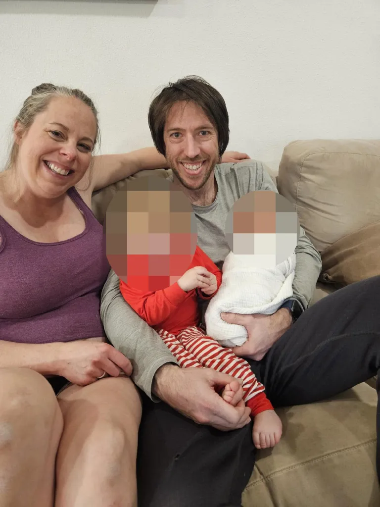 A smiling woman and a man, Patrick Theodore Barnett, sitting on a couch with two pixelated children, one in red stripes and one swaddled in white.