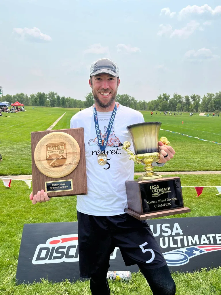 A man holding two trophies for Masters Mixed Division Champions at the USA Ultimate tournament.