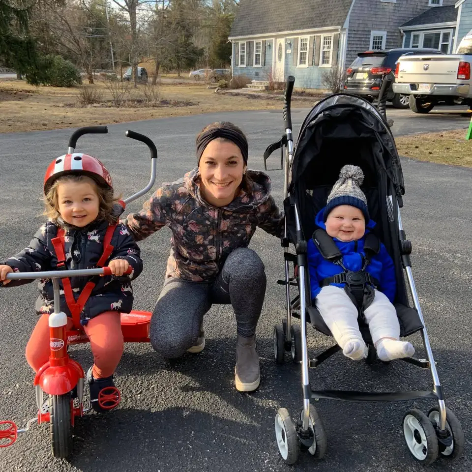 A mother with a child on a tricycle and a baby in a stroller.