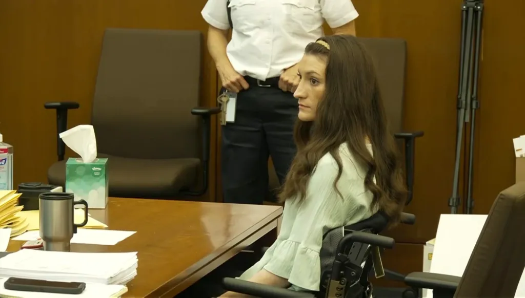 Lindsay Clancy sits in a wheelchair at a table in a courtroom during her trial.