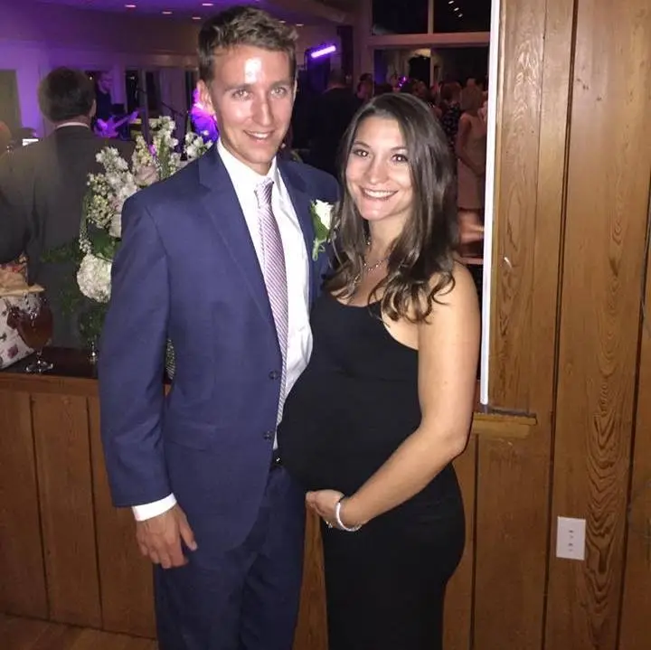 A man in a suit and a pregnant woman in a black dress smile for a photo.