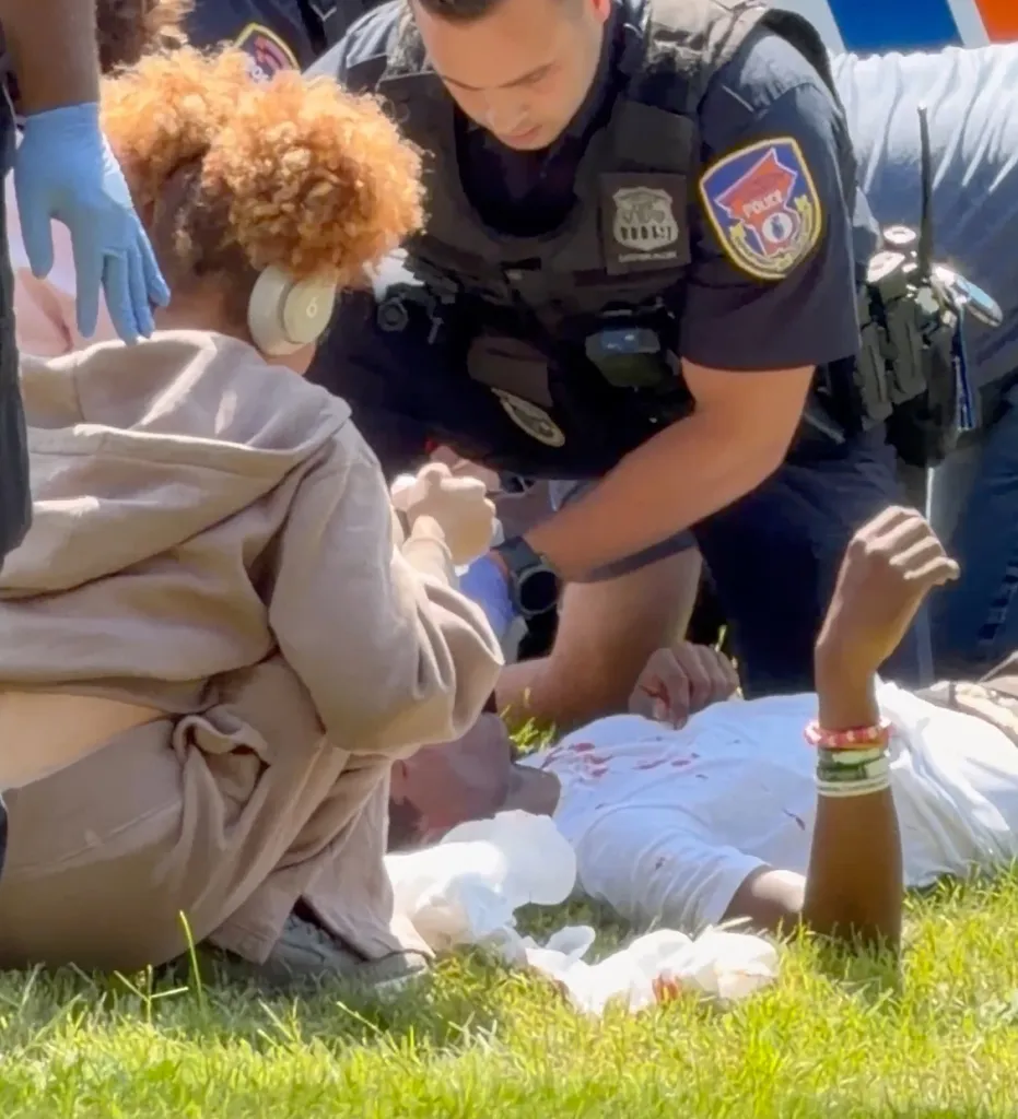 Police and others tending to a person lying on the ground with blood on their shirt.