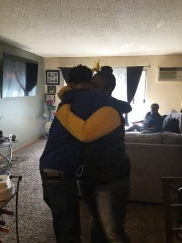 A woman and teenager hug in a living room.