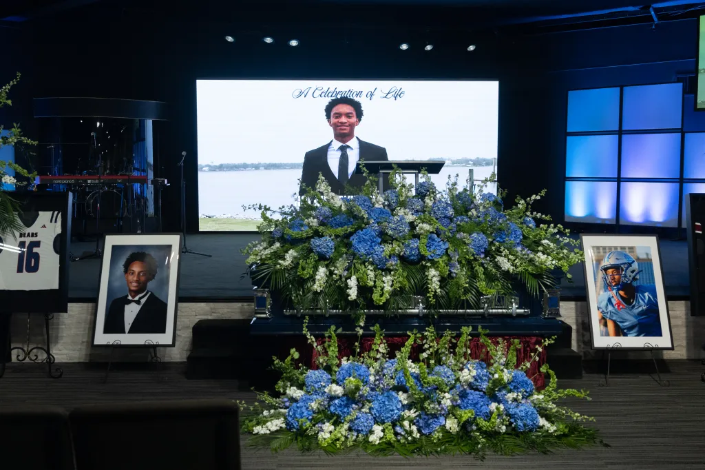 Funeral for Nolan Wells at Center Pointe Church with a casket adorned in blue and white flowers, surrounded by framed photos and a large screen displaying "A Celebration of Life."