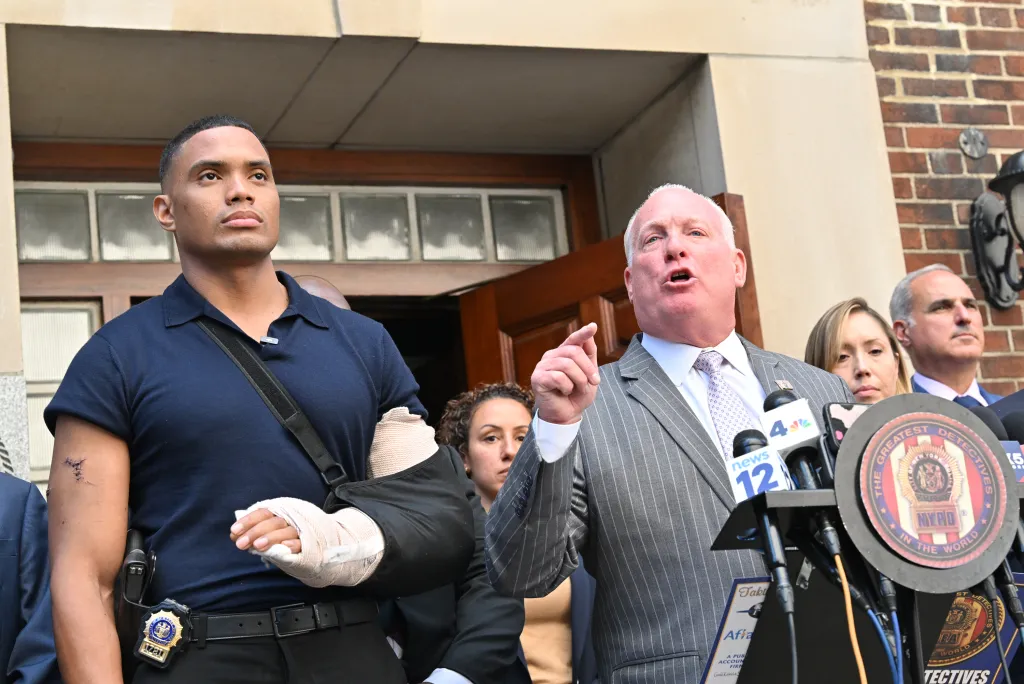 DEA President Scott Munro speaks at a press conference, joined by NYPD Detective Jose Mercedes, who wears a sling and bandages following an attack.