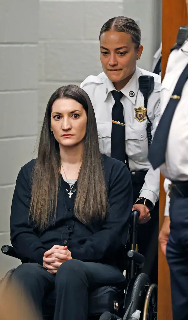 Lindsay Clancy, in a wheelchair, is pushed by a law enforcement officer in court.