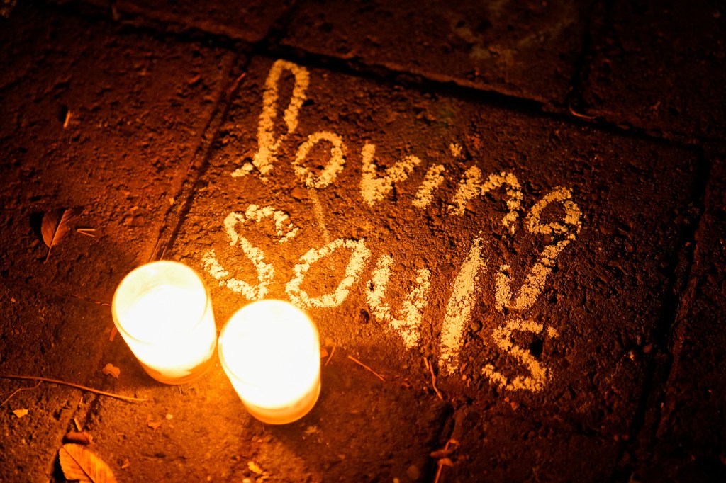 Two glowing candles and the words "loving souls" written in white chalk on the ground at a vigil.