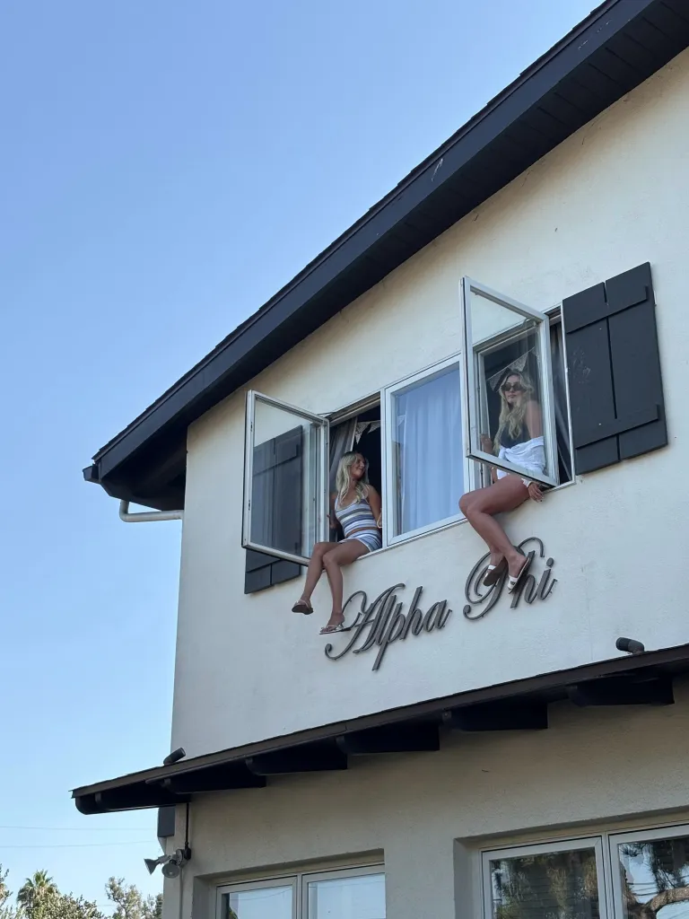 Two women sitting on the window sills of the Alpha Phi house at UCSB.