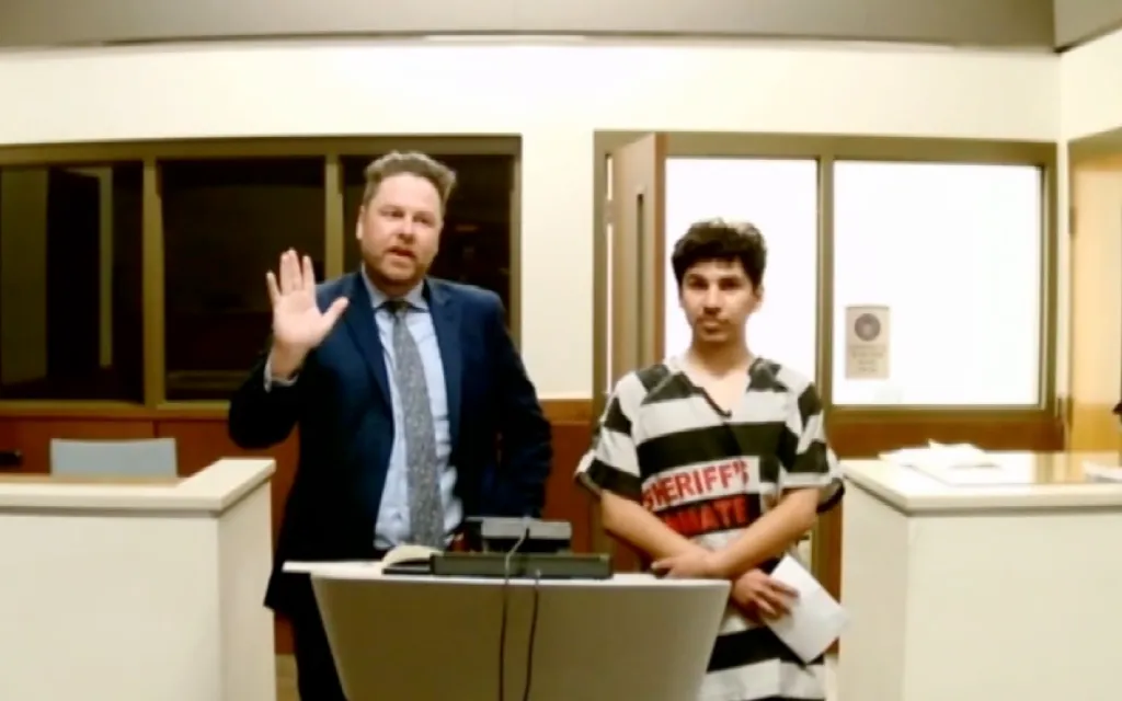 A man in a suit and tie stands next to a younger man in a striped inmate uniform in what appears to be a courtroom.