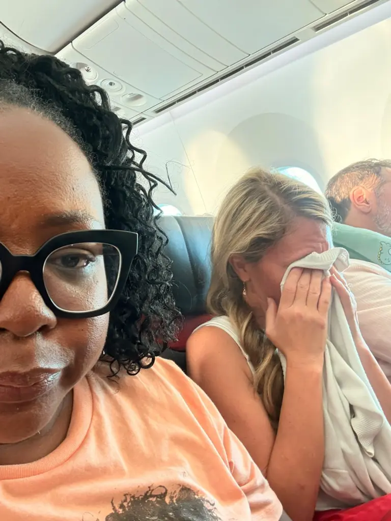 Tomiko Harvey sitting next to a passenger who is crying and wiping her eyes with a cloth during a flight.
