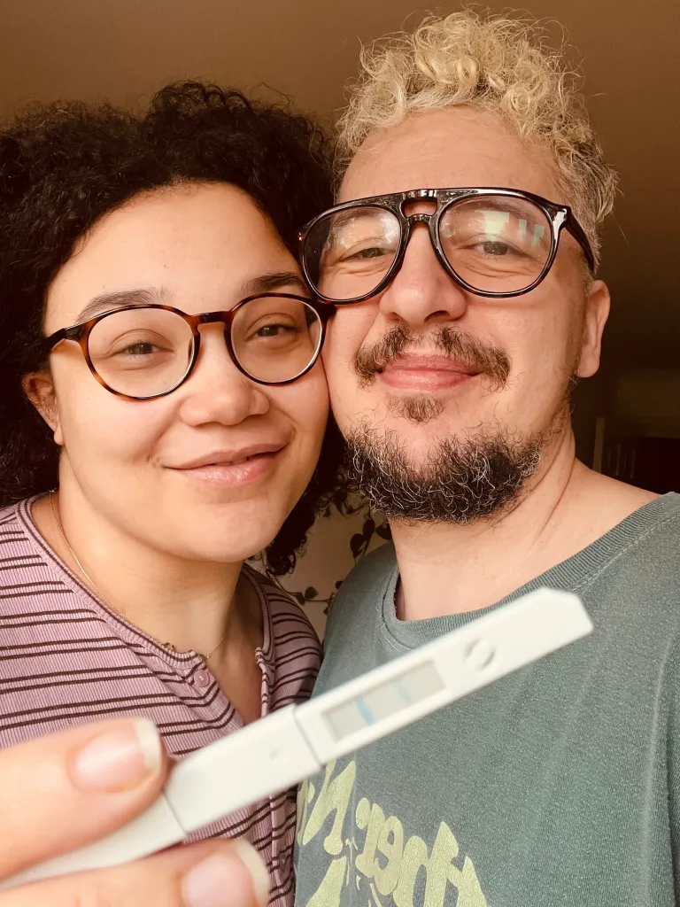 Taylor and his wife, Chloe, pose for a photo together, holding a positive pregnancy test.