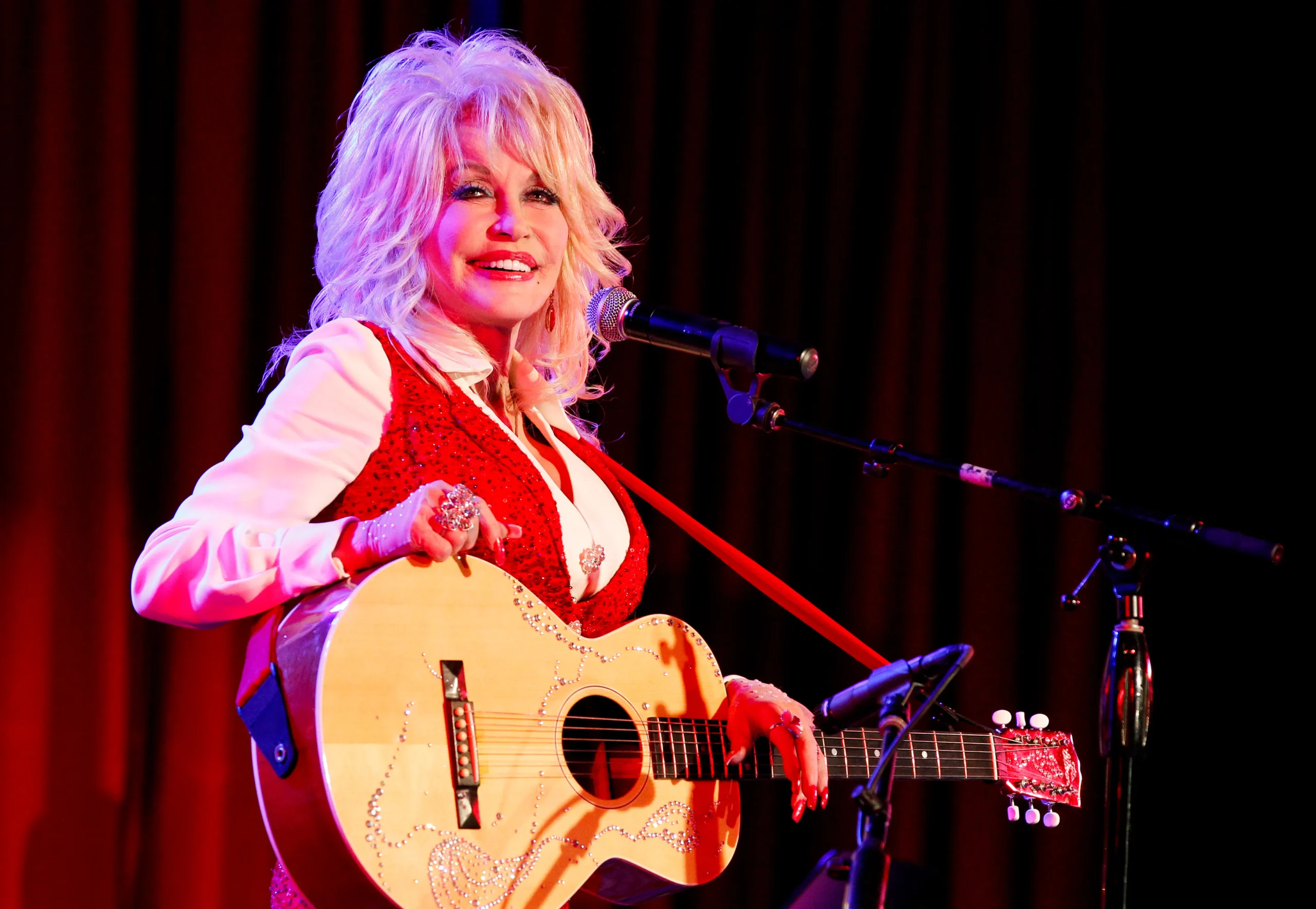 Dolly Parton performing on stage with a guitar.