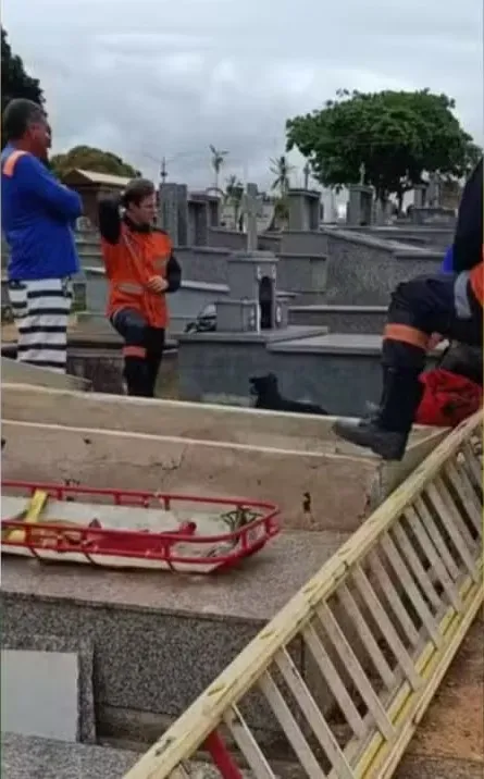 Emergency workers and bystanders stand near an open grave at a cemetery.