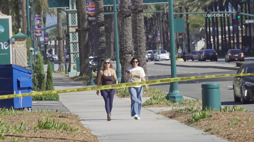 Two women walk along a sidewalk behind caution tape near a Disneyland resort.