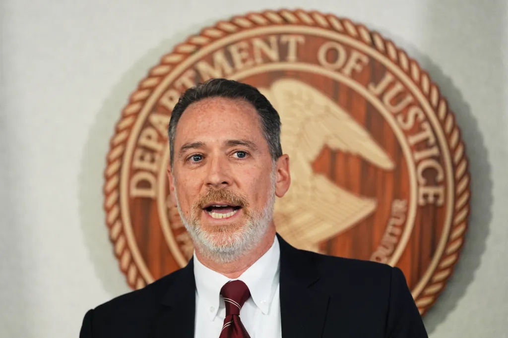 U.S. Attorney Michael J. Heyman speaks at a news conference in front of a Department of Justice seal.