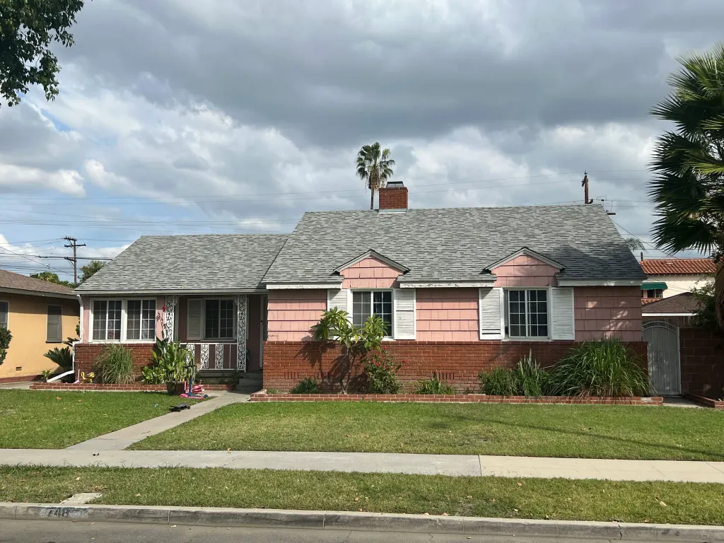 A single-story pink house with a gray shingle roof and brick base in Anaheim.