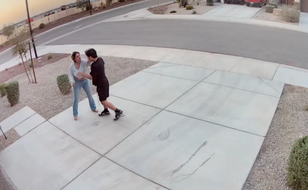 Security camera footage of a man and woman in a driveway, with the woman pushing the man back as he stumbles.