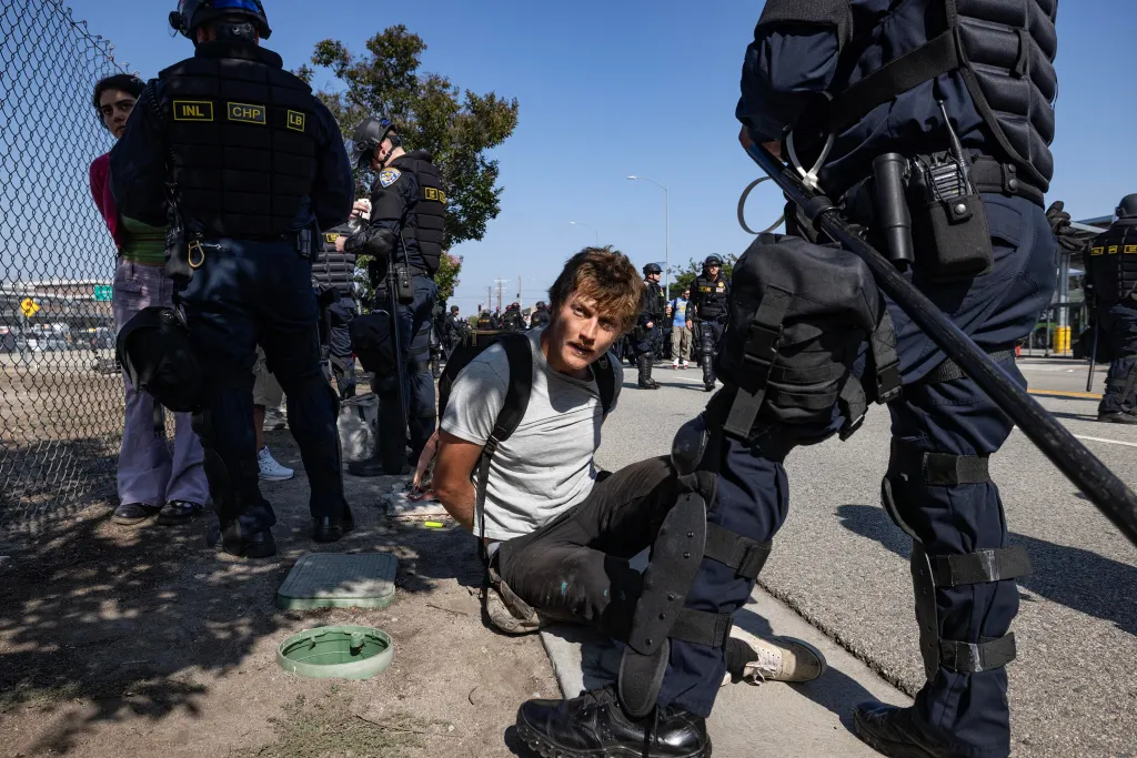 California Highway Patrol officers detain a protester sitting on the ground with his hands behind his back.