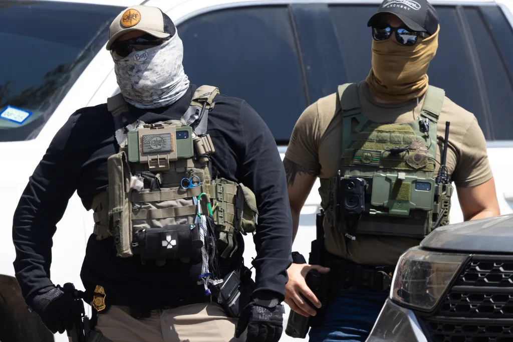 Two ICE agents wearing tactical gear and face coverings stand outside Dodger Stadium.
