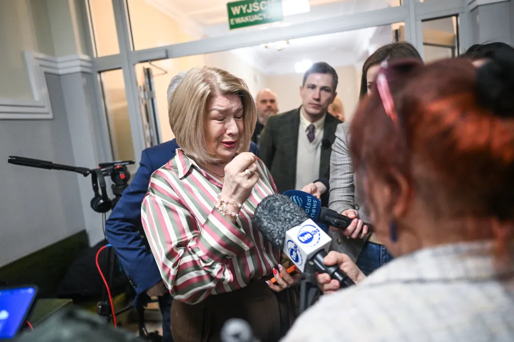 Lilianna Kupaj speaks to the press outside a court room, surrounded by journalists holding microphones.