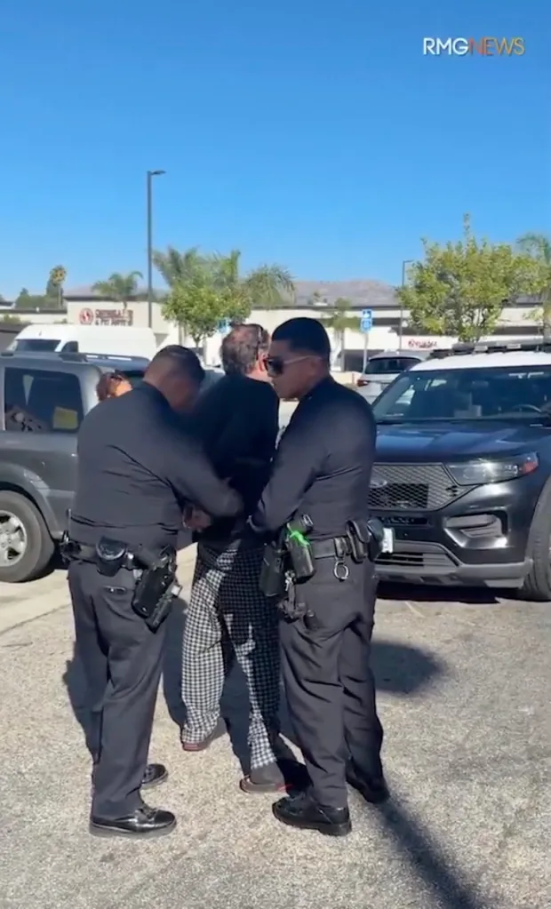 Two police officers in black uniforms handcuff a knife-wielding suspect in a parking lot.