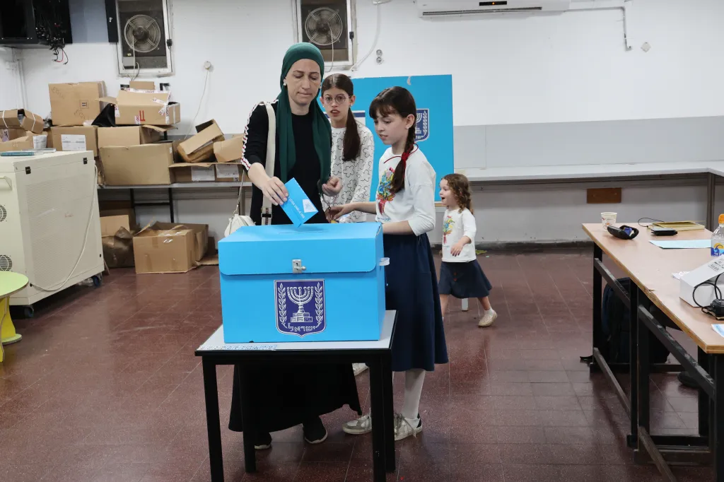 A woman casts her ballot at a polling station in Bnei Brak, central Israel, with children watching.